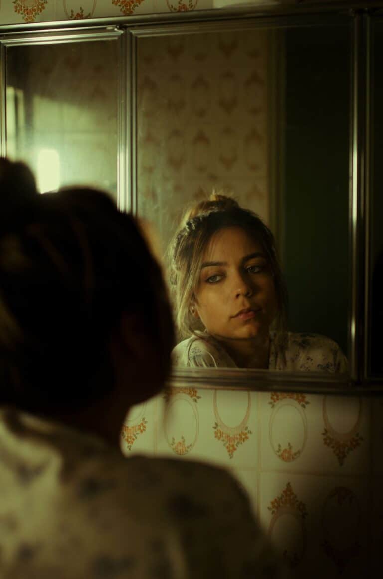 Mujer joven observando pensativa su reflejo en el espejo de un baño